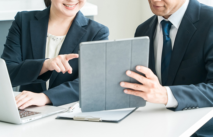 パソコンやタブレットを見て微笑んでいる社会人の写真