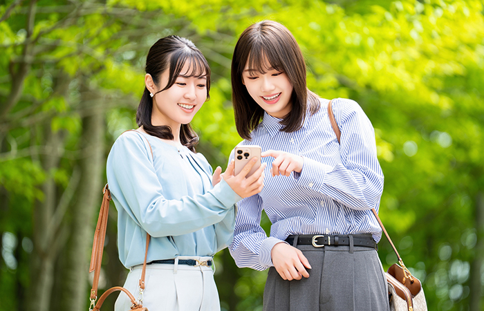 外で携帯を見て微笑んでいる女性二人組の写真